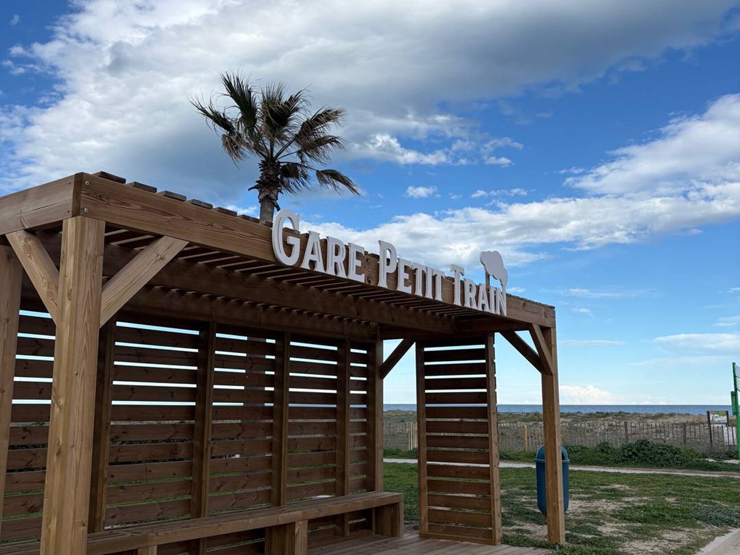 Una struttura in legno con il cartello "Gare Petit Train" e una palma sulla sommità.