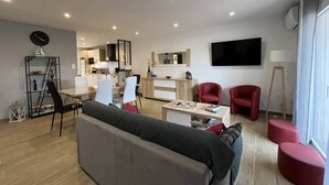 Una sala de estar moderna con un sofá, sillas rojas, una mesa de comedor y una cocina al fondo.