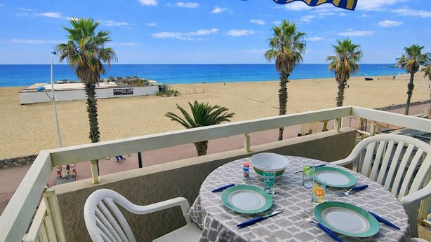 Un balcón con vistas a la playa, una mesa para dos y un toldo rayado.