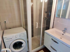A compact bathroom with a washing machine, a glass-enclosed shower, and a vanity with a mirror. - 2-Room Apartment Sea View in Canet-Plage (Canet-Plage)