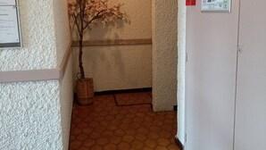 Un pasillo con piso de baldosas, una planta en maceta y carteles informativos en las paredes.