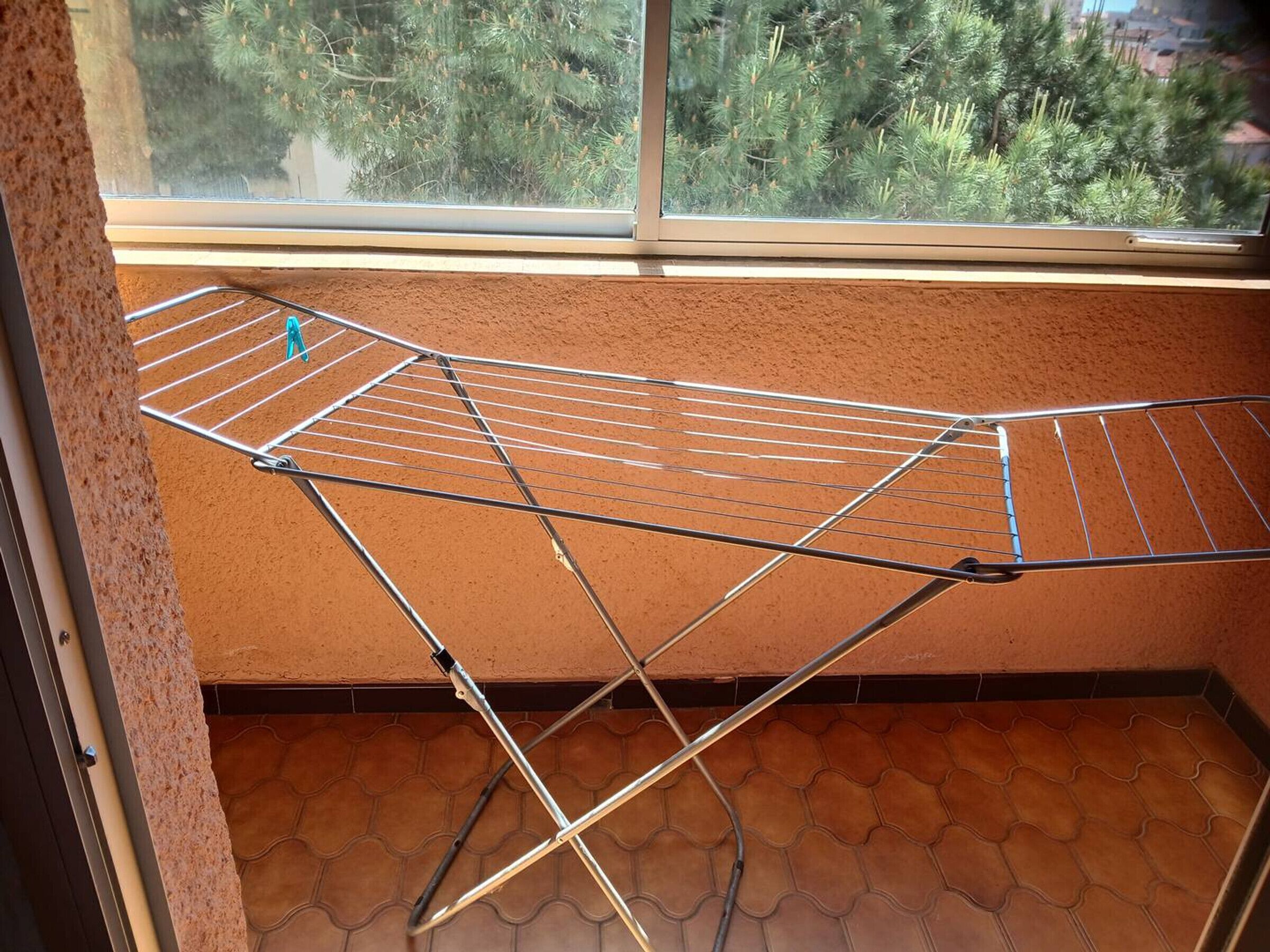 A room with a window, a metal drying rack, and a tiled floor.