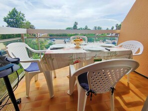 A balcony with a table set for two, white plastic chairs, and a view of a road and greenery. - 2* Apartment with Balcony and Parking - Port Canet (Canet-Plage)