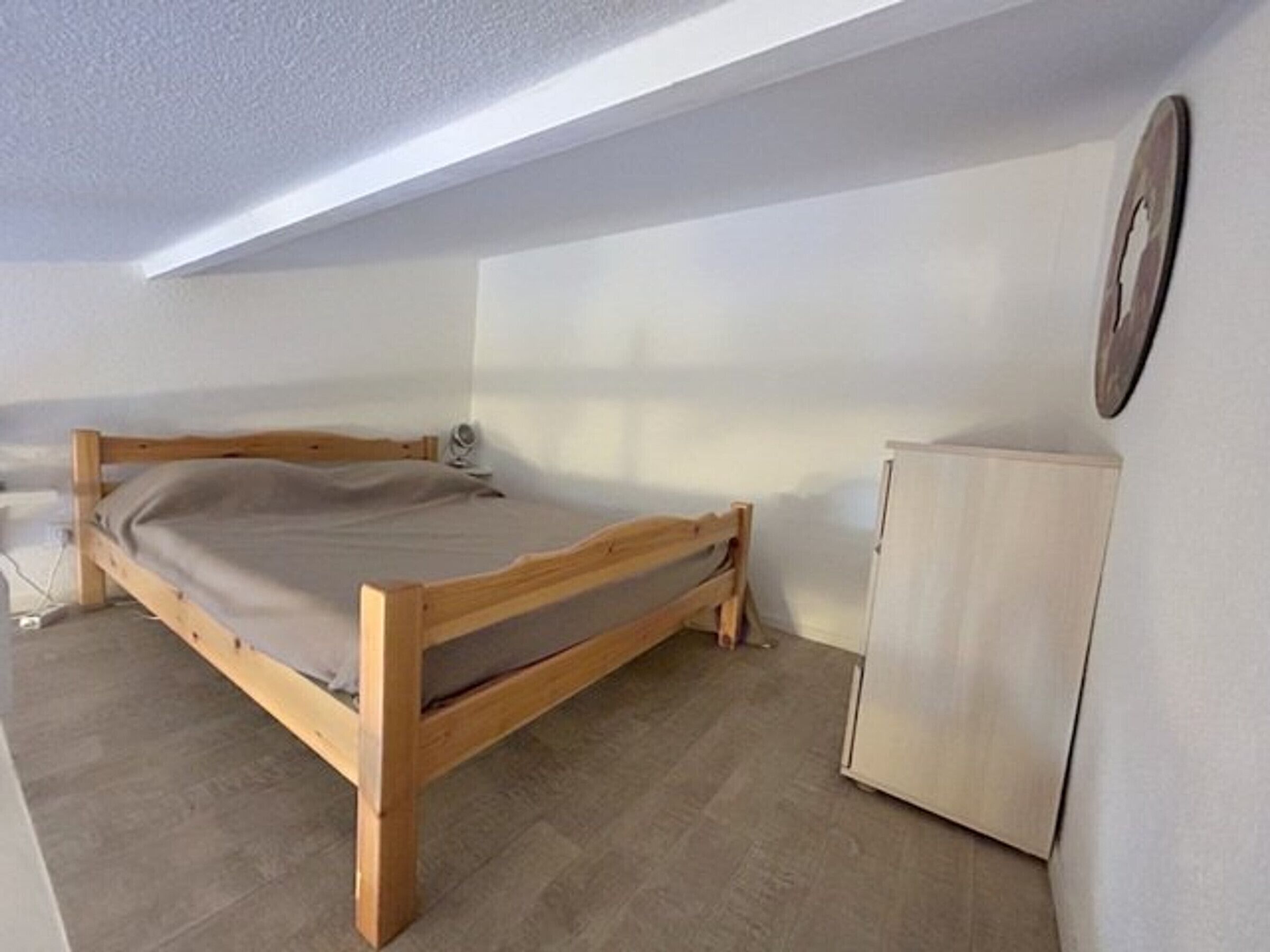 Une chambre à coucher avec un lit en bois, une petite armoire et un ventilateur de plafond.