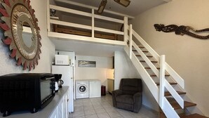 Ein kompakter Wohnraum mit Küchenzeile, Waschmaschine, Stuhl und einer Treppe.