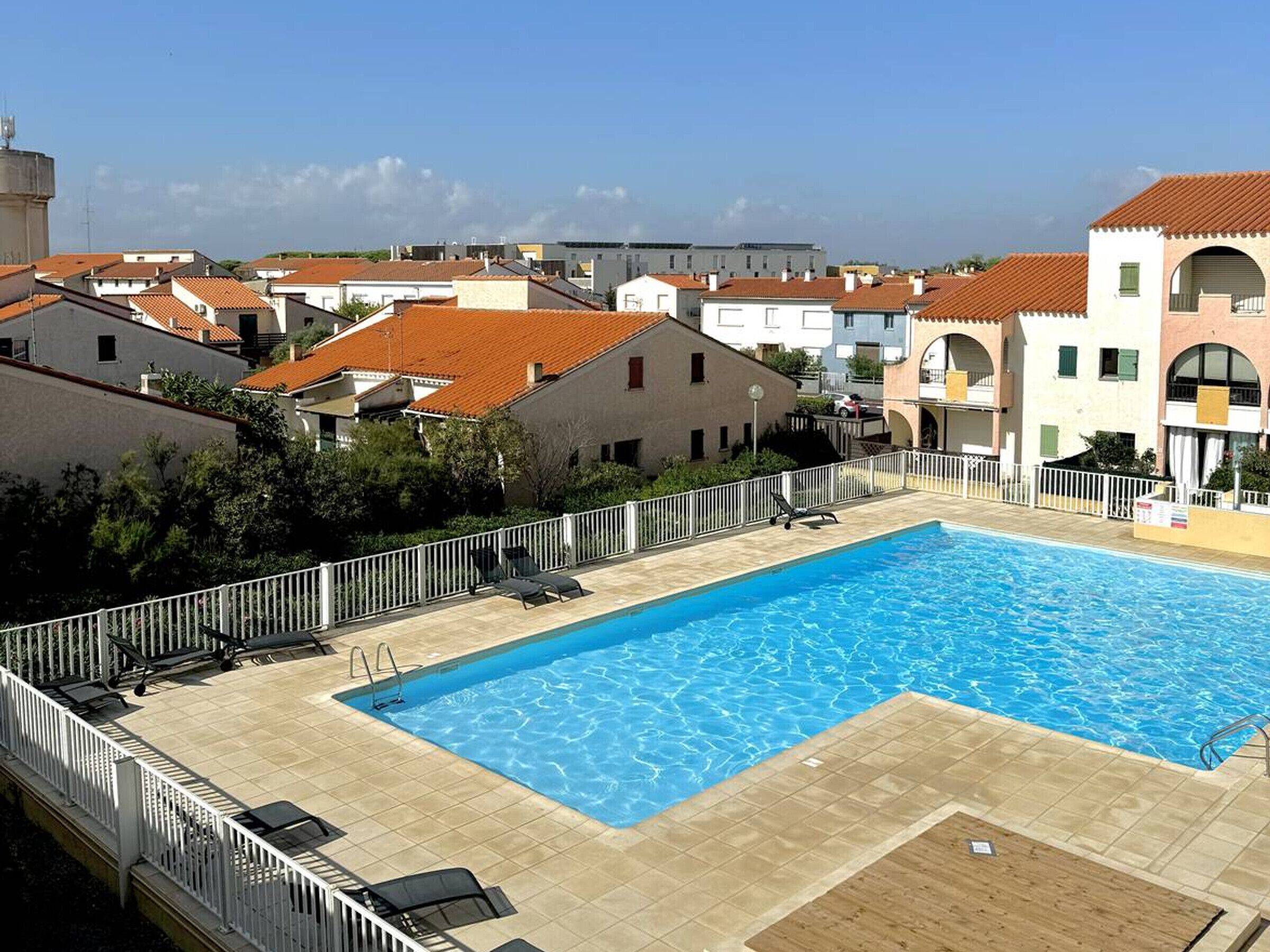 Une piscine rectangulaire avec une terrasse carrelée, entourée d’une clôture blanche.