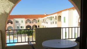 A balcony with a pool view, a round table, and chairs. - Charming T2 with mezzanine and parking in Le Barcarès (Le Barcarès)