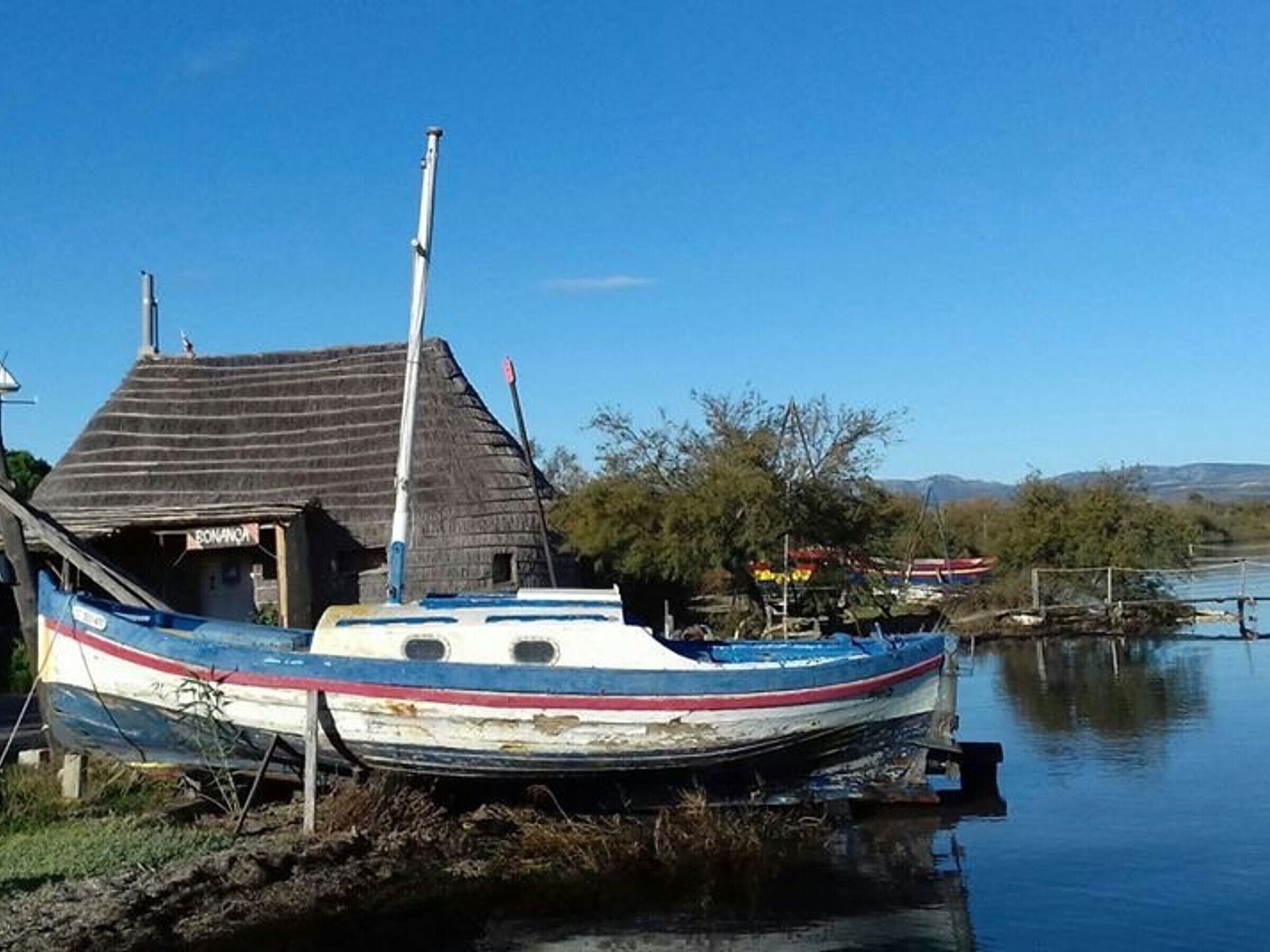 Una barca ormeggiata vicino a una casa con tetto di paglia.