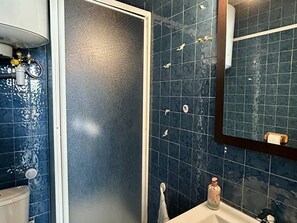 A bathroom with blue tiles, a white sink, a mirror, and a shower area. - Cozy Apt Near Beach with Terrace, Parking & AC – Le Barcarès (Le Barcarès)