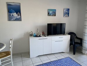A living room with a white cabinet, a flat-screen TV, a small table, and a chair. There are three framed pictures on the wall. - 3-room apartment, port view, for 6 in Canet-Plage (Canet-Plage)