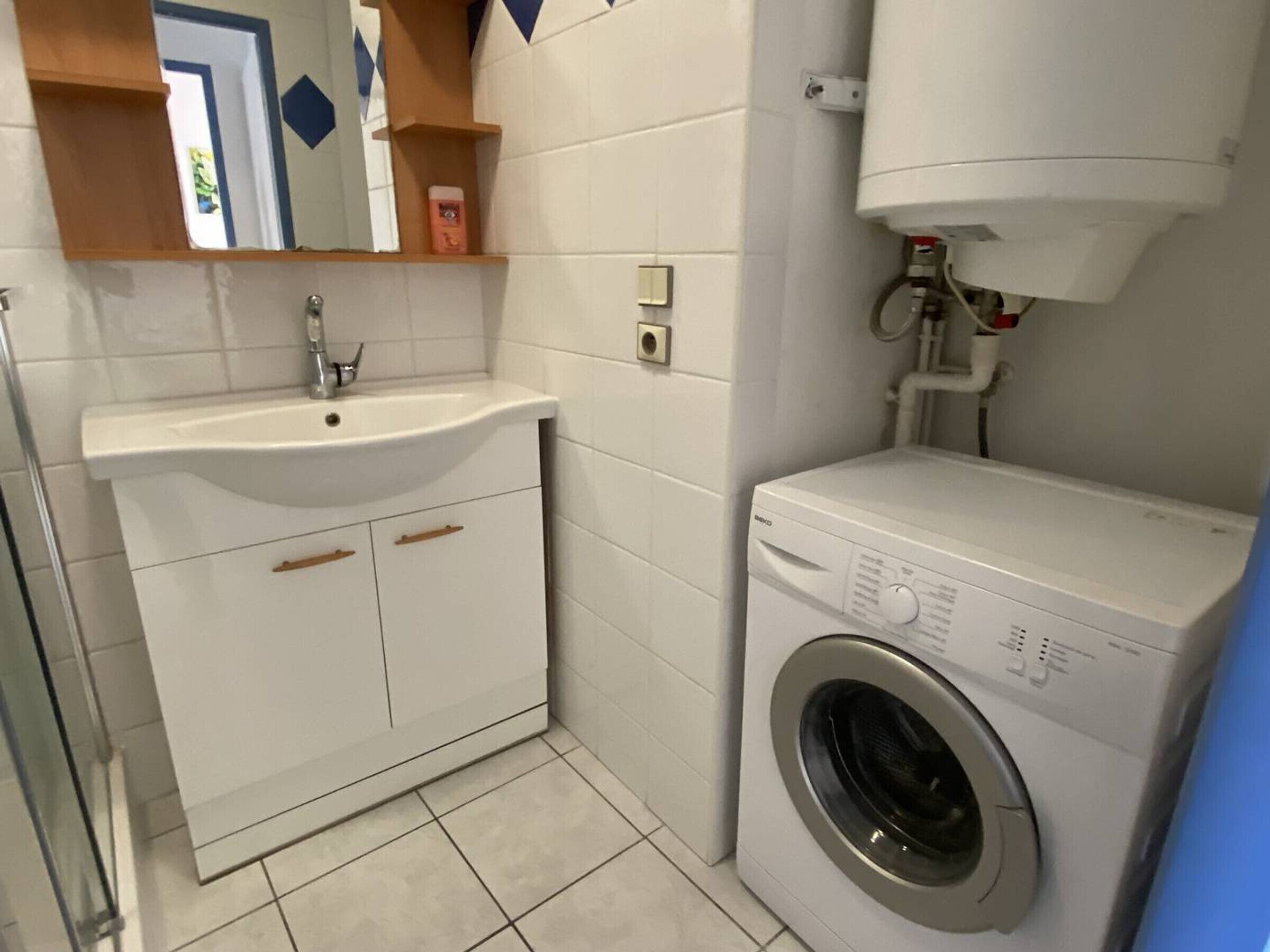 Une petite salle de bain comprenant un lavabo, un lave-linge et un miroir.