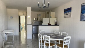 Cozinha moderna com armários brancos, micro-ondas e geladeira. Há uma área de jantar com mesa e cadeiras.