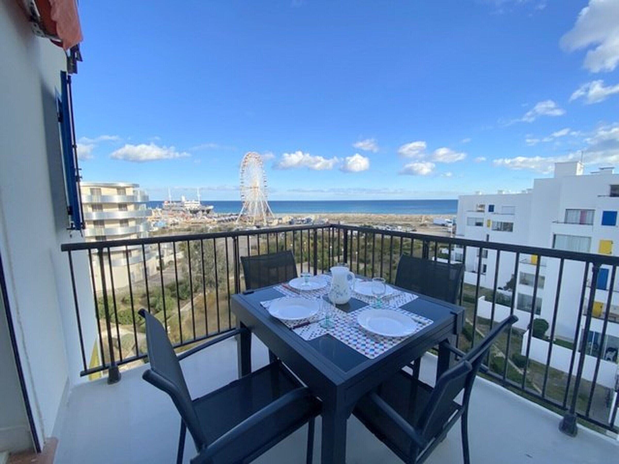 Een balkon met een tafel voor twee, met uitzicht op een strand en een reuzenrad.
