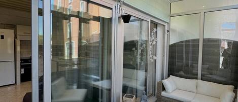 Een modern zitgedeelte buiten met rieten meubels en een glazen deur naar een keuken.