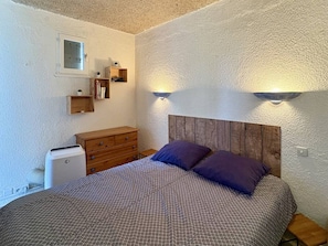 A bedroom with a bed, wooden dresser, and wall-mounted shelves. - Air-conditioned studio near beach and shops with terrace (Le Barcarès)