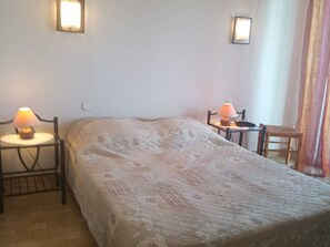 A bedroom with a bed, two bedside tables with lamps, a chair, and a window with curtains. - Air-conditioned apartment, renovated, 4 people, near beach and shops (Canet-en-Roussillon)