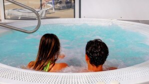 A hot tub with two people sitting inside, a pool visible outside, and a window reflecting the scene. - Cozy mobile home with terrace for 4 in Bénodet (Bénodet)