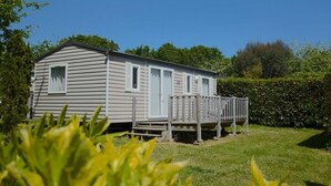 Une maison mobile de plain-pied, dotée d’un porche et entourée de verdure.