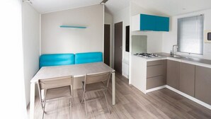 Une cuisine de taille réduite, équipée d’une cuisinière à gaz, d’un évier et d’une fenêtre avec des stores.