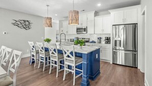 A modern kitchen with white cabinets, a stainless steel refrigerator, and a blue island. - Almost Heaven on Sunset-Pool-Walk to Beach (Murrells Inlet)