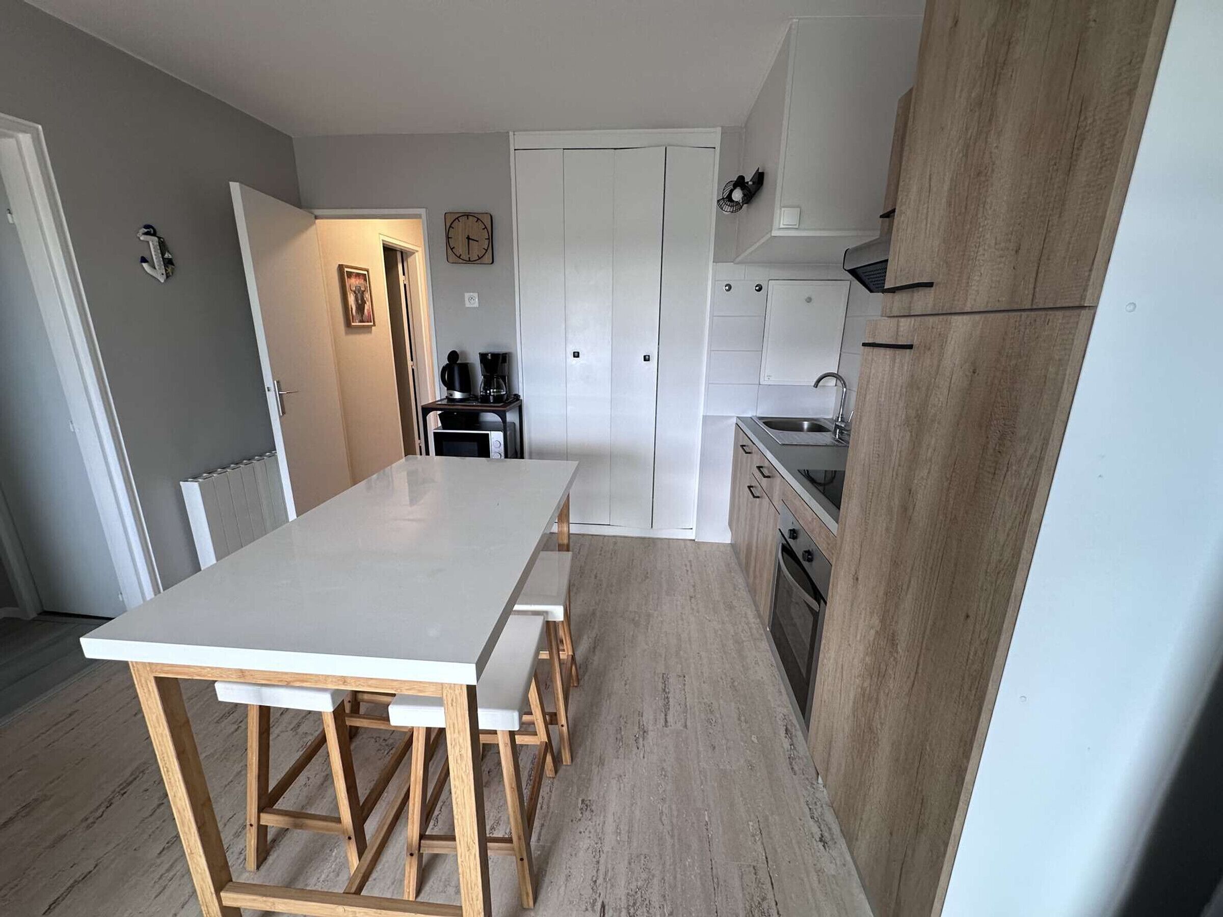 Une cuisine de taille réduite avec un îlot central, des meubles blancs et un plancher en bois.