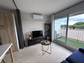 A modern living room with a flat-screen TV, a small table, and a sofa. - Beautiful renovated 2-room apartment with air conditioning and private parking for 4 in Port Camargue (Le Grau-du-Roi)