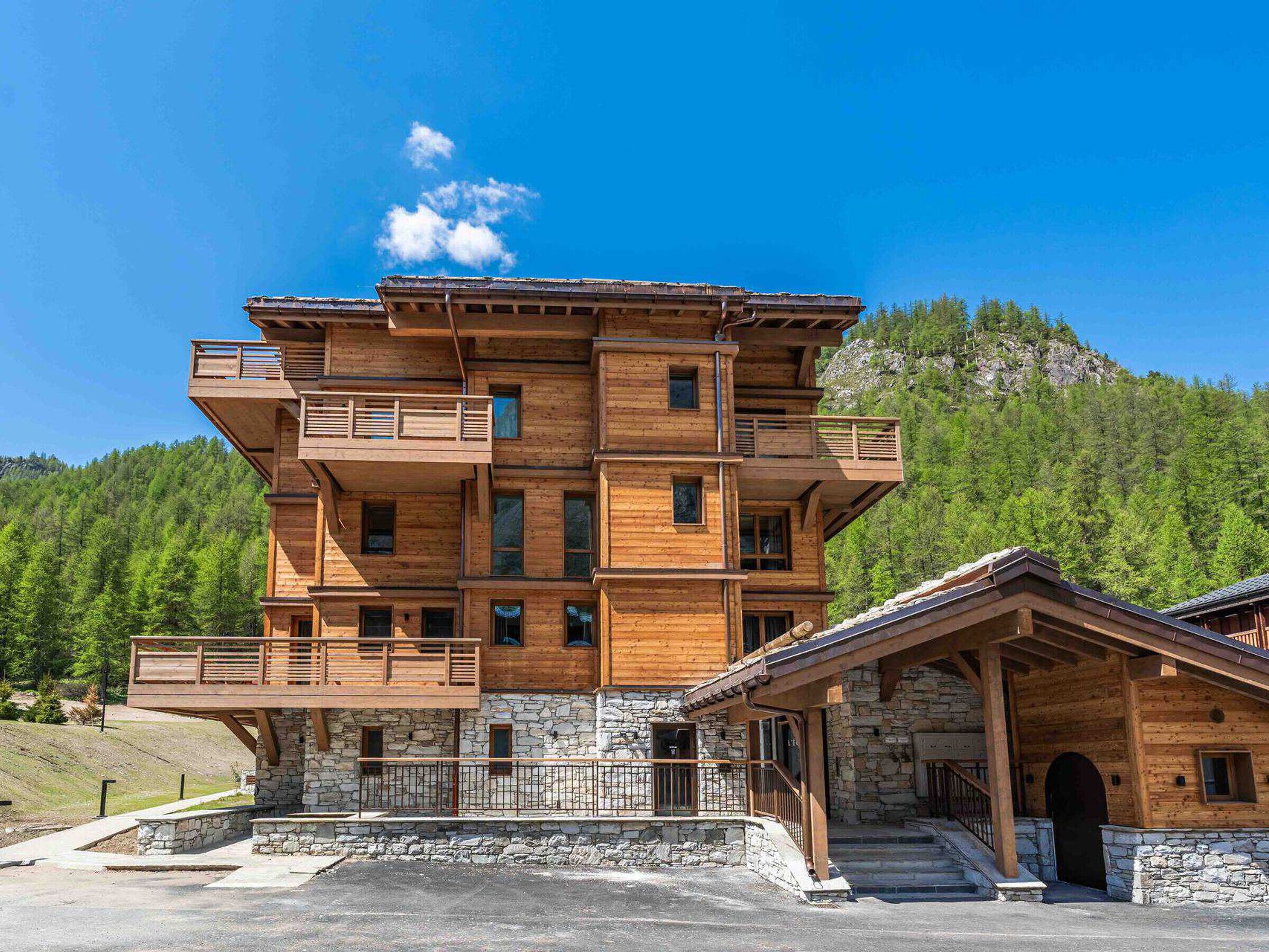 Un immeuble en bois à plusieurs étages, doté de balcons, d’une base en pierre et d’une petite structure adjacente.