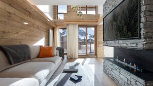 Ein modernes Wohnzimmer mit Kamin aus Stein, einem großen Fernseher und einer Couch mit Kissen.