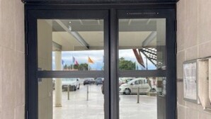 A building entrance with a glass door, a tiled floor, and a view of parked cars and a flag outside. - Charming T2 by the sea for 4 pers, terrace with view (Canet-Plage)
