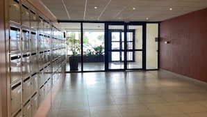A spacious hallway with metal mailboxes on the left and a glass door leading outside. - Charming T2 by the sea for 4 pers, terrace with view (Canet-Plage)