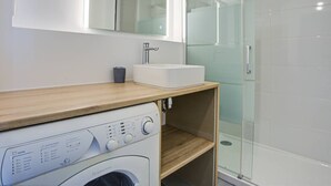 A modern bathroom with a built-in washing machine, a sink, and a glass shower enclosure. - Canet Beach modern renovated T2, near sea (Canet-en-Roussillon)