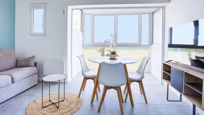 A modern living room with a sofa, a dining table with chairs, a TV, and large windows offering a view of the beach. - Canet Beach modern renovated T2, near sea (Canet-en-Roussillon)