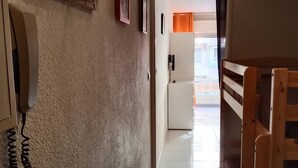 A hallway with a telephone on the left, a door at the end, and a wooden bench on the right. - Studio for 4 near the sea in Canet-en-Roussillon (Canet-en-Roussillon)