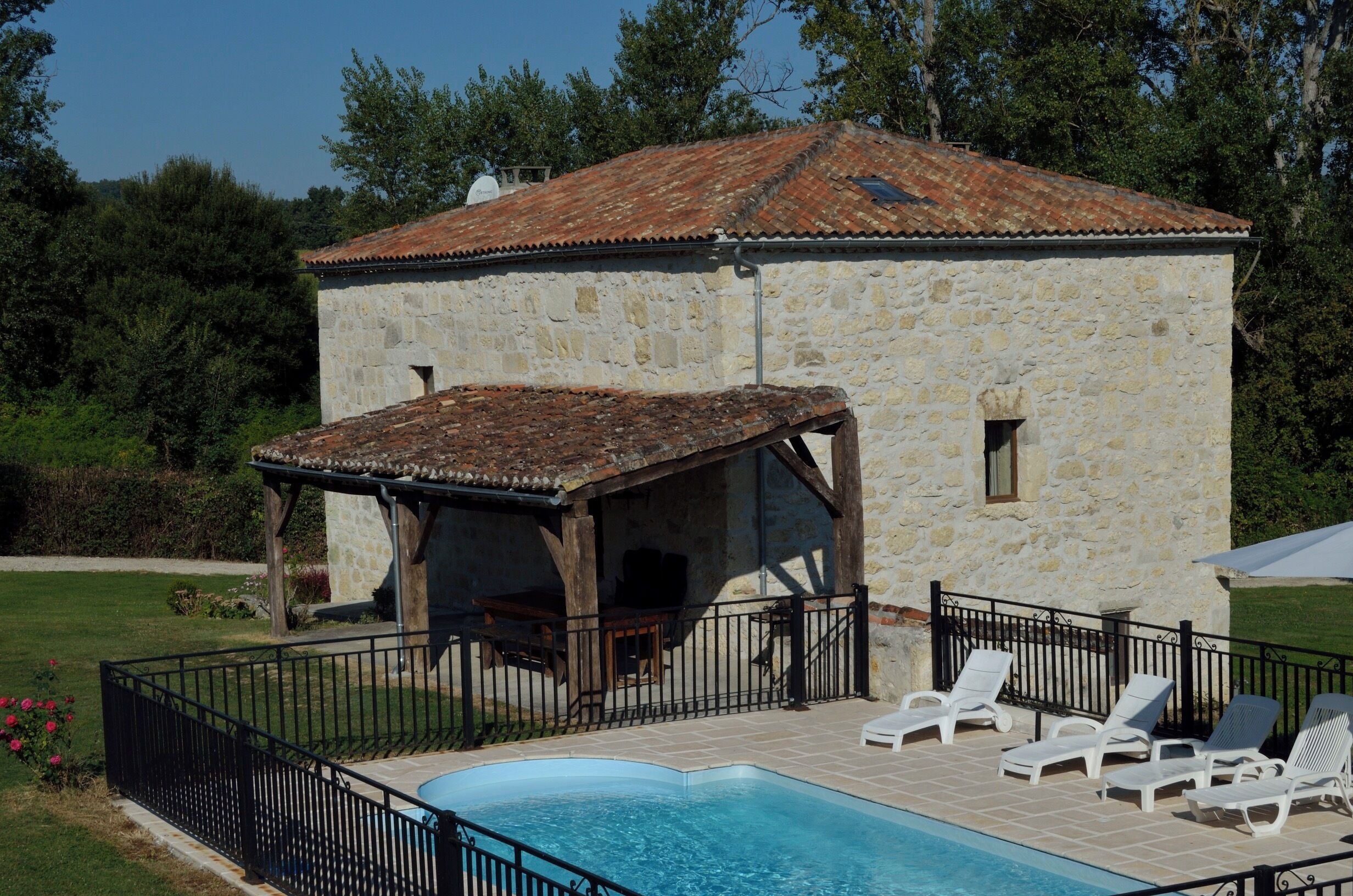 Un edificio de piedra con techo de tejas, piscina con sillones de descanso y patio amurallado.