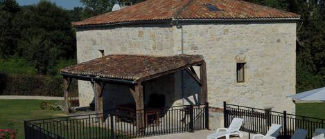Un edificio de piedra con techo de tejas, piscina con sillones de descanso y patio amurallado.