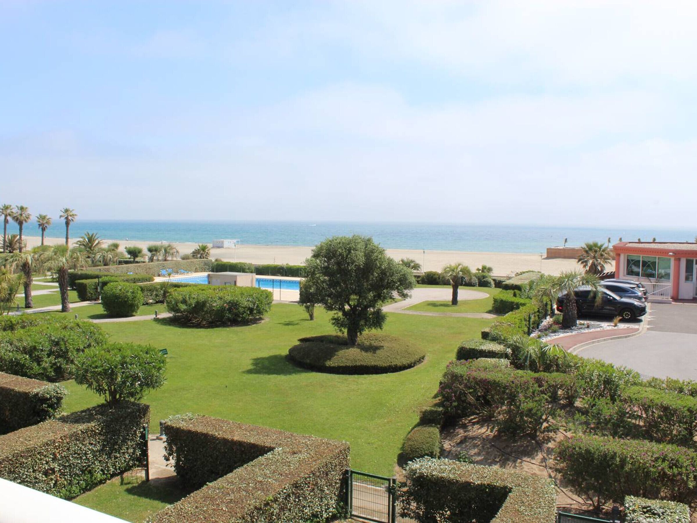 A view of a landscaped garden with a pool, palm trees, and a beach in the background.