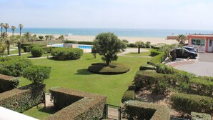 A view of a landscaped garden with a pool, palm trees, and a beach in the background. - Luxurious air-conditioned apartment with great view and secure parking (Canet-Plage)