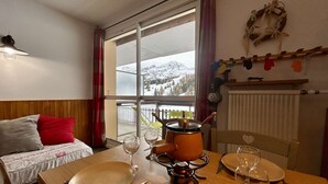 A cozy dining area with a table set for two, a wooden table, and a view of a snowy mountain through a large window. - Ski-In Studio for 4 pers. with Parking (Le Dévoluy)
