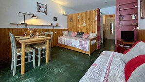A cozy room with a wooden bed, a dining table with chairs, and a TV. - Ski-In Studio for 4 pers. with Parking (Le Dévoluy)