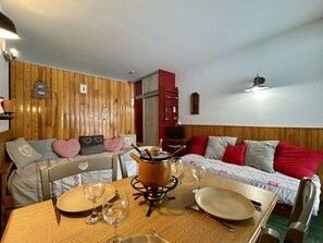 A cozy room with a wooden wall, a bed with red and grey pillows, a dining table set with plates, glasses, and a pot on a stove. - Ski-In Studio for 4 pers. with Parking (Le Dévoluy)