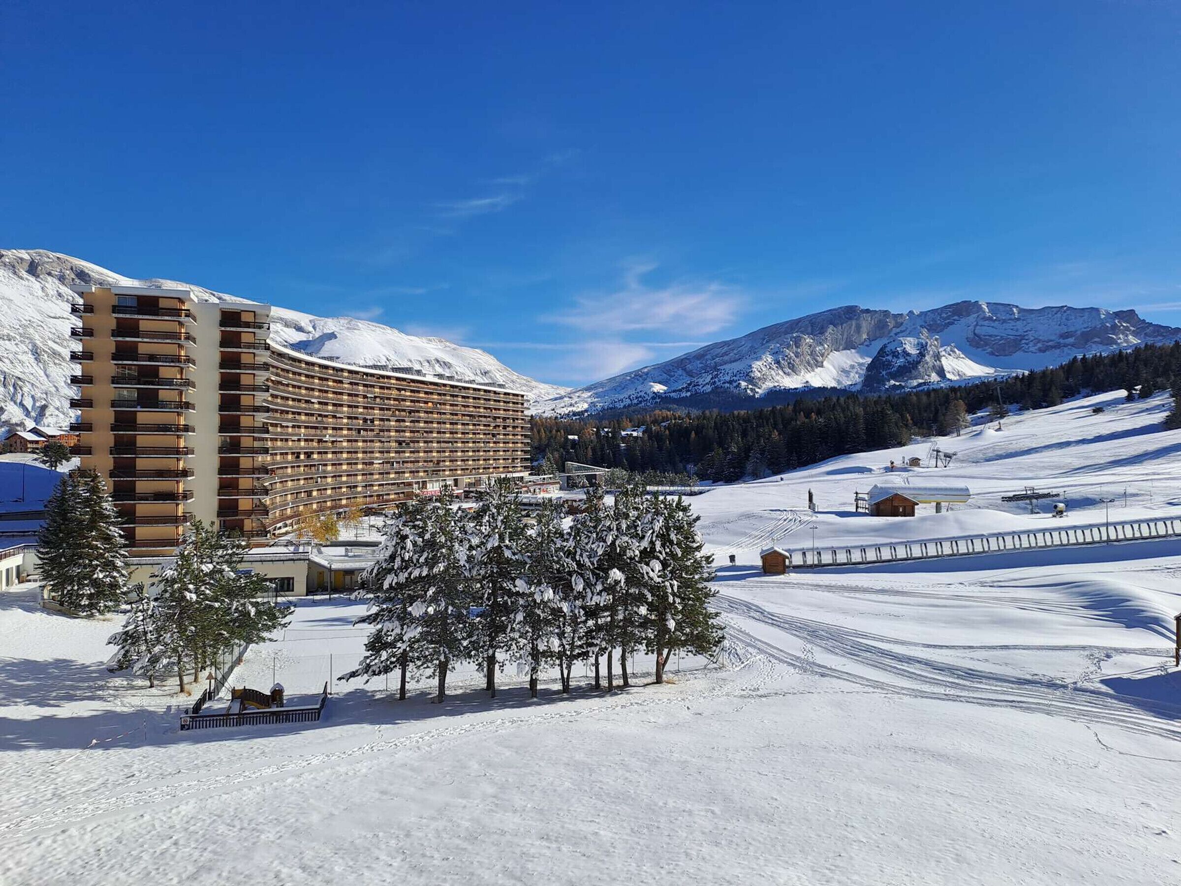 Hotel amb façana corba, múltiples balcons i vista a muntanyes cobertes de neu.