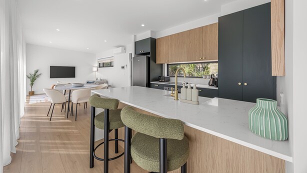 A modern kitchen with a large island, dark cabinets, and a green vase.