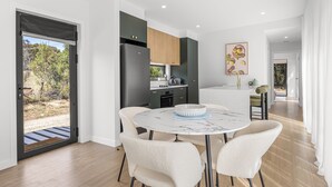 A modern kitchen with dark cabinets, a white marble table, and a view of the outdoors.
