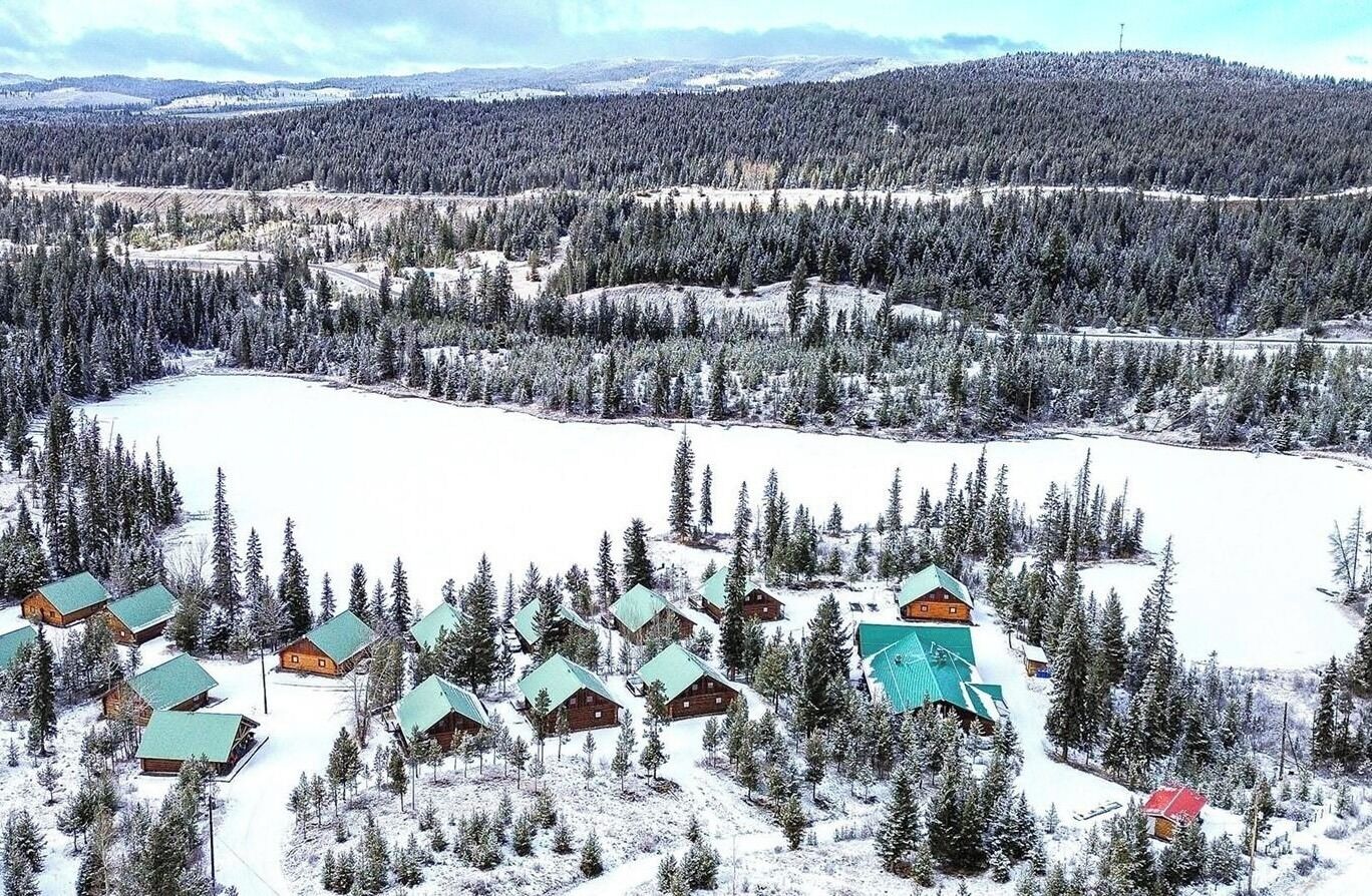 A snow-covered landscape with cabins clustered around a lake, surrounded by dense forests.