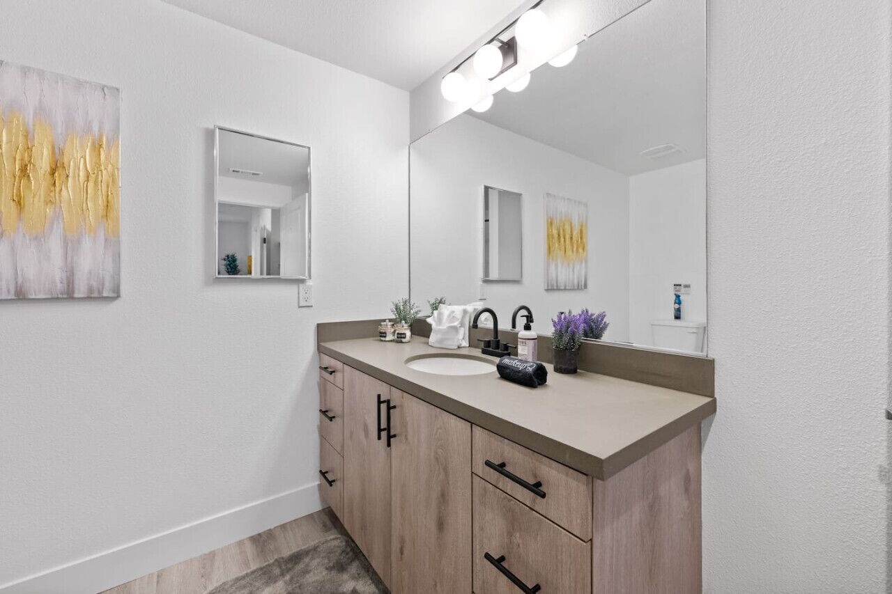 A modern bathroom with a large mirror, a sink, and wooden cabinets.