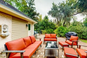 A patio with outdoor furniture, a covered grill, and a house with a stone facade. - Dog-friendly Home With Central AC, Washer/dryer & Spacious Backyard - Near Beach (St. Simons Island)