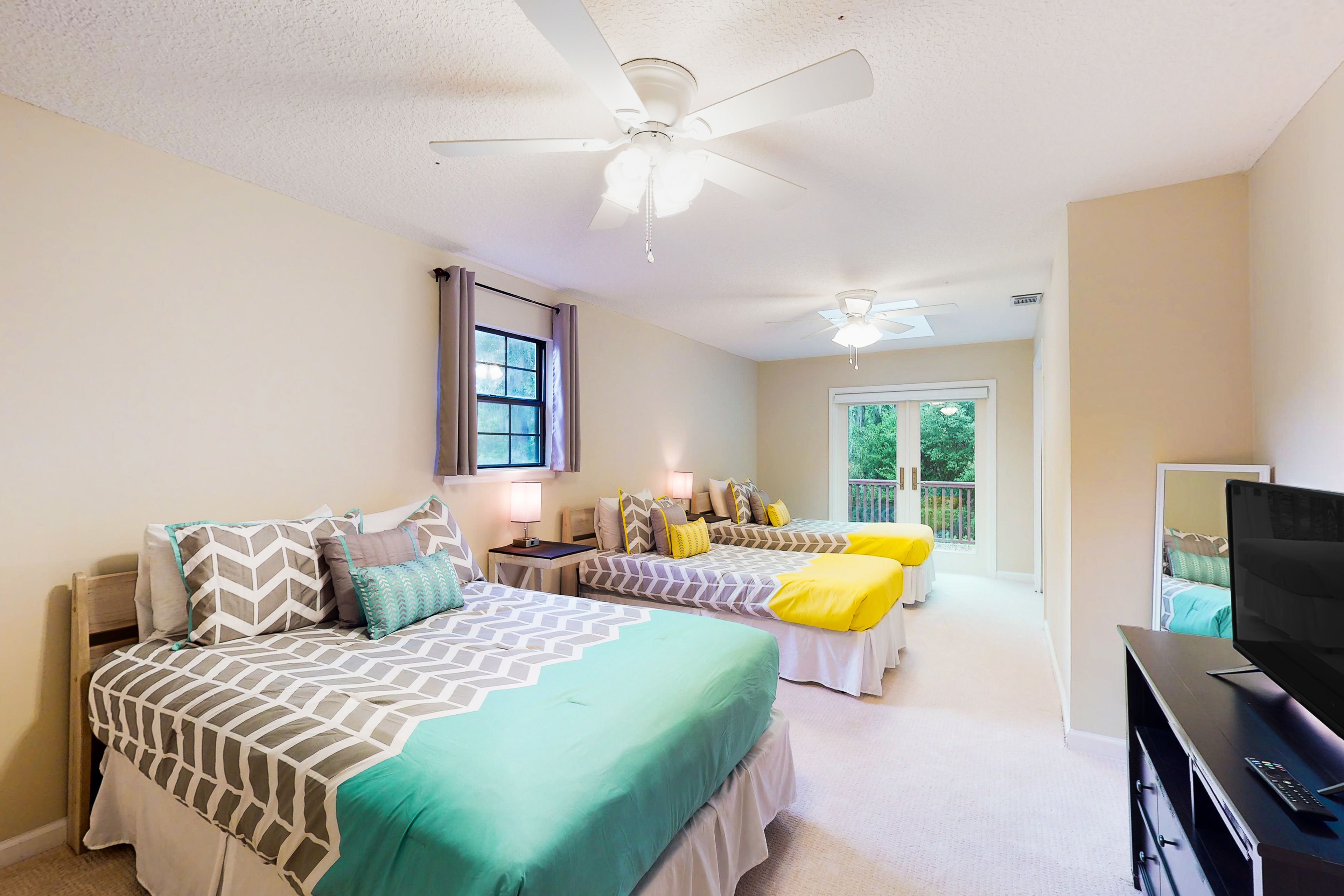 A bedroom with two beds, a ceiling fan, a TV, and a window with curtains.