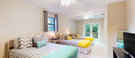 A bedroom with two beds, a ceiling fan, a TV, and a window with curtains.