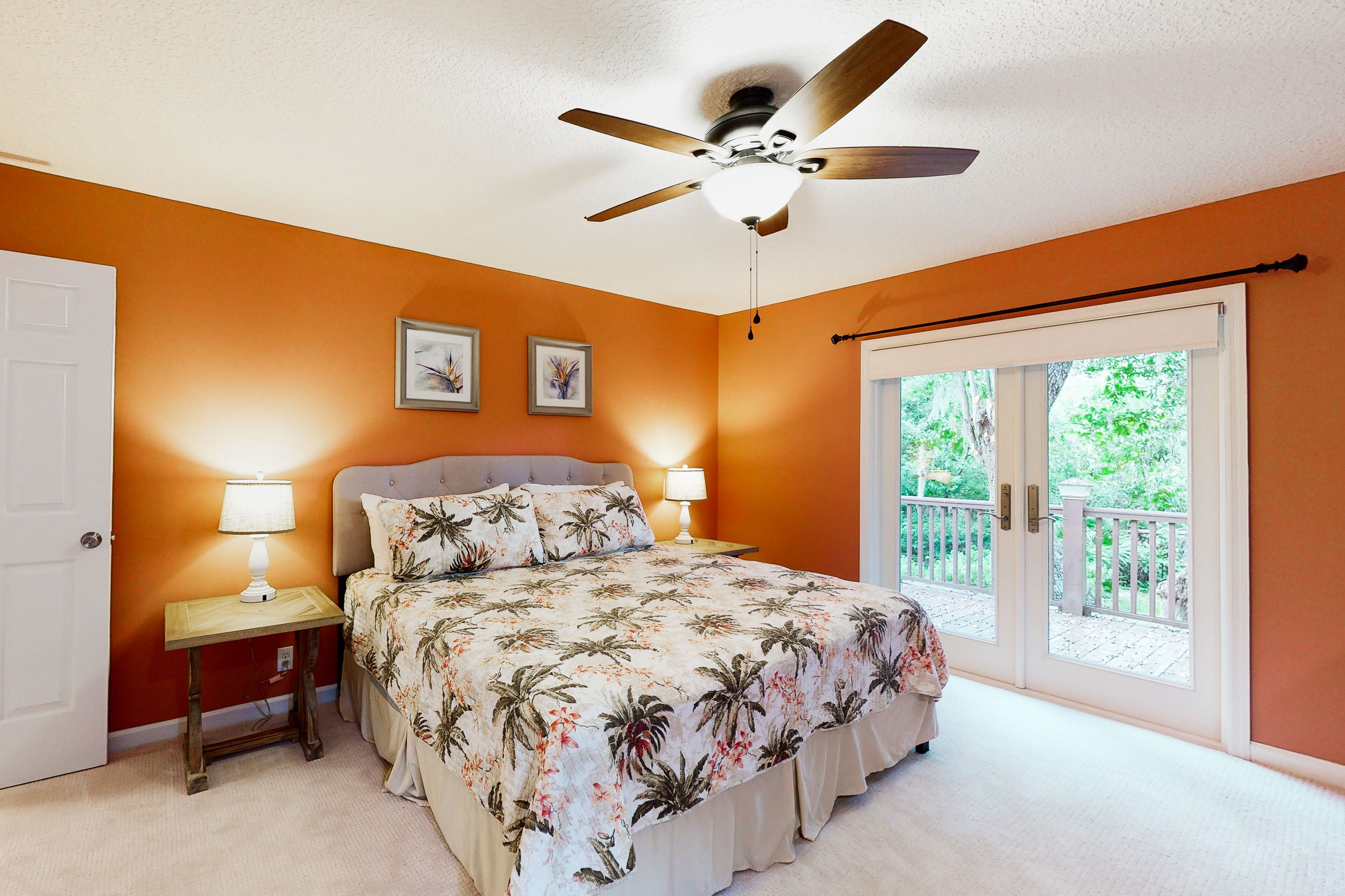 A bedroom with a bed, a ceiling fan, a nightstand with a lamp, and a sliding glass door to a balcony.