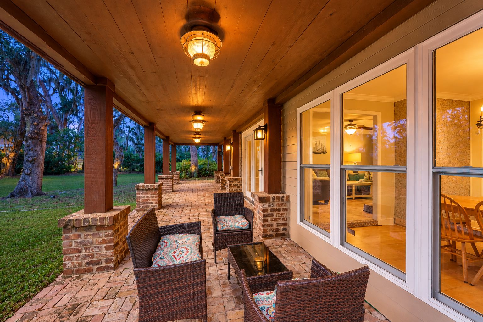 An outdoor covered patio with wicker furniture and brick accents, leading to a glass door entrance.